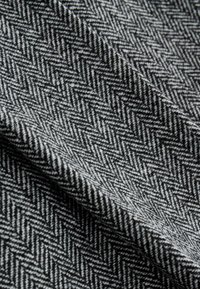 Hahnentrittmusterstoff in Schwarz und Weiß, mit strukturiertem Erscheinungsbild, das eine diagonale Webart und weiche Oberfläche zeigt.