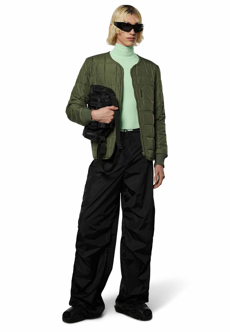 Giacca bomber imbottita verde oliva, dolcevita menta, pantaloni neri larghi e borsa nera testurizzata. Gli accessori includono occhiali da sole neri angolari.