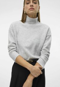 Pull à col roulé gris en tissu doux et texturé avec des manches longues. Porté avec une jupe noire, comportant une boucle de ceinture ovale dorée.