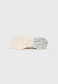 Semelle d'une sneaker beige avec une texture de grip et une section en caoutchouc gris au niveau du talon, isolée sur un fond blanc.