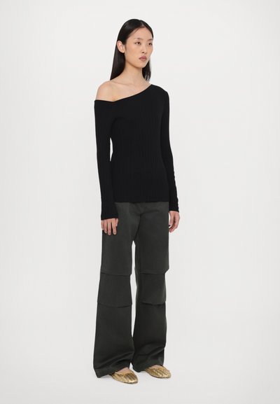 Zwart geribbeld gebreid langemouwen off-shoulder top gecombineerd met donker groene wijde cargo broek en gouden platte schoenen met een gestructureerd patroon.