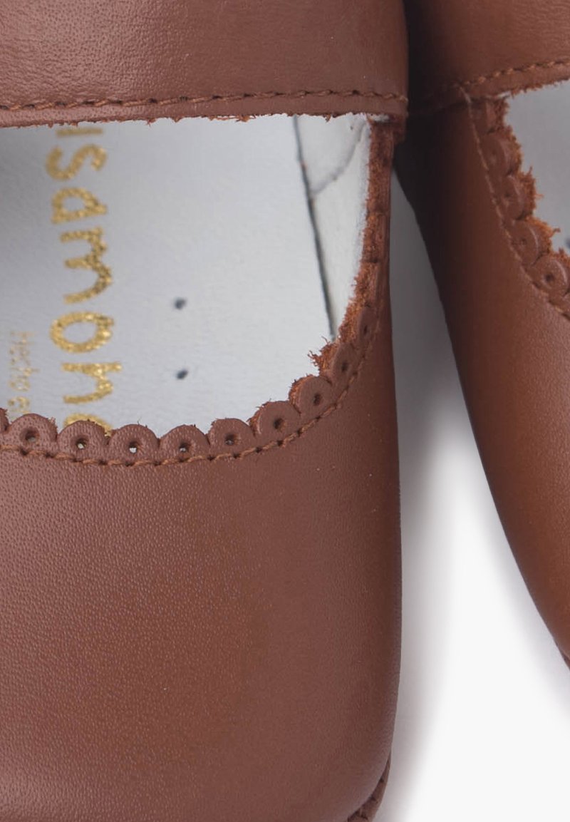 Brown leather shoes with scalloped edges around the openings. Interior features white lining with gold logo text. Smooth texture.