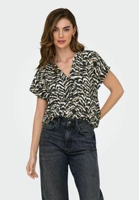 Kortärmad blus i svart och beige djurtryck, med en djup V-ringning och en lös passform, bärs tillsammans med högmidjade svarta jeans.