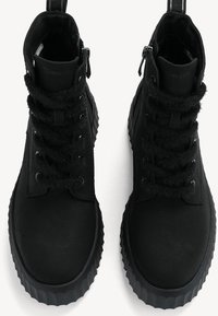 Schwarze High-Top-Stiefel aus strukturiertem Synthetikleder. Merkmale sind flauschige schwarze Schnürsenkel, ein seitlicher Reißverschluss und eine dicke, geriffelte Sohle.