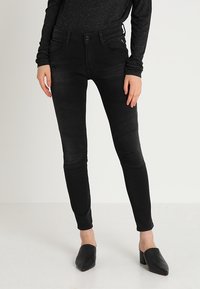 Jeans ajustados de denim negro con detalles en los paneles de las rodillas. Presentan un cierre de botón, cinco bolsillos y una cintura de altura media. Textura suave y forma ajustada.