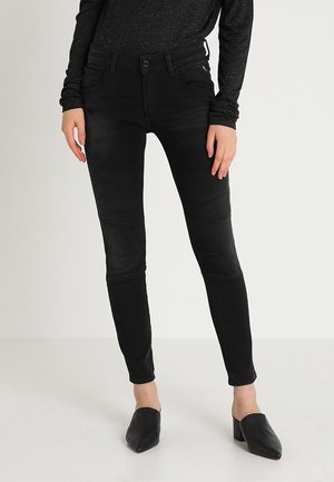 Jeans ajustados de denim negro con detalles en los paneles de las rodillas. Presentan un cierre de botón, cinco bolsillos y una cintura de altura media. Textura suave y forma ajustada.
