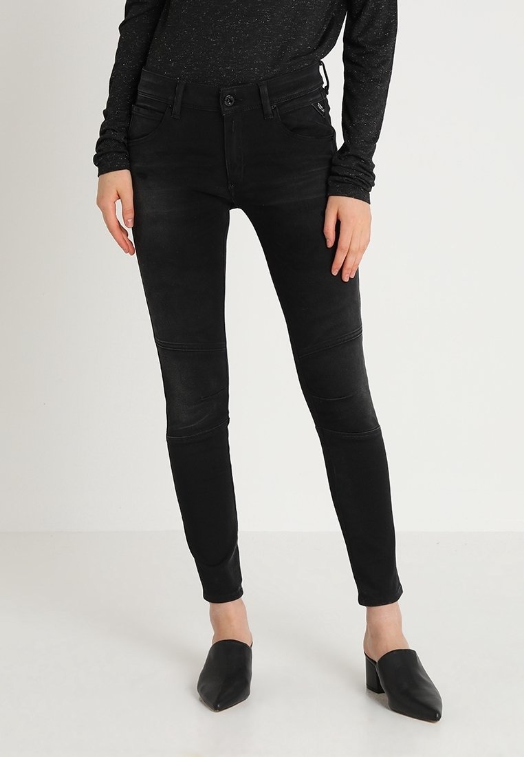Jeans ajustados de denim negro con detalles en los paneles de las rodillas. Presentan un cierre de botón, cinco bolsillos y una cintura de altura media. Textura suave y forma ajustada.