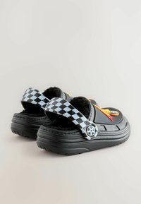 Black slip-on shoes with a fuzzy interior, featuring a checkered strap, red accents, and a circular logo design on the upper section.