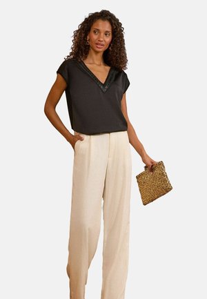 Schwarzes, kurzärmliges Top mit V-Ausschnitt und strukturierter Borte; kombiniert mit cremefarbenen, weiten Hosen und einer kleinen, geflochtenen goldenen Clutch.
