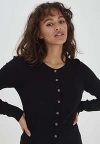 Cardigan nero realizzato in tessuto morbido, con scollatura rotonda, chiusura frontale con bottoni metallici e tasche laterali.