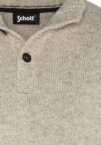 Beige gebreide trui met een opgevouwen kraag, voorzien van een half-knopenlijst en een gestructureerd patroon. Zwarte knopen voegen detail toe.