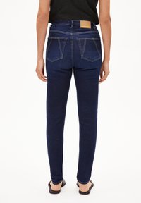 Jean skinny en denim bleu foncé, avec des poches arrière cousues, une étiquette en cuir à la taille et un design ajusté.