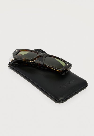 Occhiali da sole rettangolari con montatura tartarugata e lenti scure, appoggiati su una custodia protettiva in pelle nera su uno sfondo chiaro.