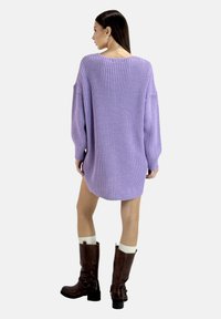 Oversized paarse gebreide trui jurk met een ribbelige structuur, lange mouwen, ronde halslijn en zijopeningen, gecombineerd met bruine kniehoge laarzen.