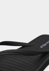 Μαύρο ανάγλυφο σανδάλι σαγιονάρας με λεπτά λουράκια και ελαφριά υποστήριξη καμάρας, σε απλό λευκό φόντο.