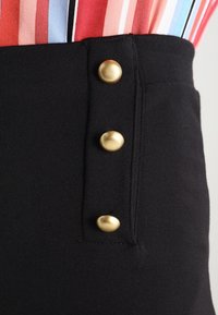 Czarne spodnie z wysokim stanem, z trzema złotymi guzikami po bokach, charakteryzujące się gładką fakturą materiału i dopasowanym krojem.