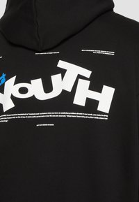 Felpa nera con cappuccio caratterizzata da grande scritta bianca "youth", testo bianco più piccolo con virgolette e dettagli grafici blu. Il materiale sembra morbido e texturizzato.