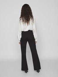 Black flared trousers with a fitted waist, paired with a white long-sleeve blouse. The trousers feature a smooth texture and a clean design.