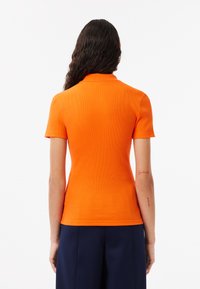 Orange kortärmad polo skjorta med ribbad textur, med en klassisk krage och en figursydd siluett, bärs med marinblå byxor.