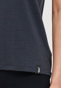 Navy blue sports shirt, lightweight fabric, smooth texture, curved hem, features a small brand tag with white logo detail at the bottom.