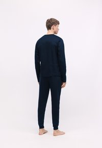 Conjunto de loungewear azul marino hecho de tela suave, que incluye una parte superior de manga larga y pantalones con puños elásticos, visto desde la parte de atrás.