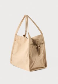 Bézs vászon bevásárlótáska egyszerű, szögletes formával, két fogantyúval, zsinóros záródással és egy első zsebbel további tároláshoz.