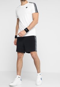 Vitt idrottströja med svart logotyp, svarta shorts med sidostreck och vita sneakers. Inkluderar handledsstöd för extra funktionalitet.