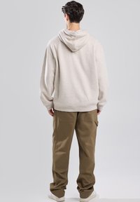 Hellgrauer Kapuzenpullover mit lockerer Passform, kombiniert mit khakifarbenen Cargo-Hosen mit Seitentaschen, vor einem schlichten Hintergrund.