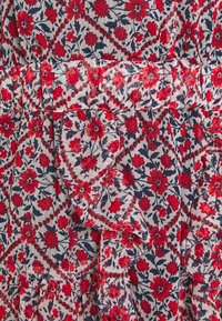 La tela con estampado floral presenta flores rojas sobre un fondo azul marino, con bordes rizados y diseños geométricos en contraste.