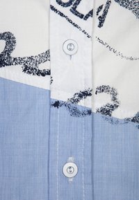 Hemd mit Knöpfen in einem weißen und hellblauen Farbschema, mit einem strukturierten blauen Stoff und einem grafischen schwarzen Druckmuster.