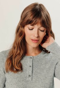 Grijze geribbelde gebreide top met een ronde halslijn, knoopdetails en lange mouwen. Het materiaal heeft een zachte textuur, ontworpen voor comfort.