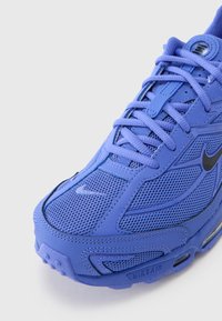 Plava sportska cipela izrađena od mrežastih i sintetičkih materijala, zaobljenog vrha, s vezicama i vidljivim Nike Air jastučićem.