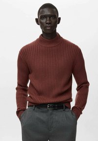 Donkerrode ribgebreide trui met een hoge hals en lange mouwen, gecombineerd met grijze, op maat gemaakte broek en een zwarte riem. Gestructureerde stof.