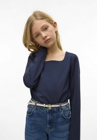 Granatowa bluzka z długim rękawem i kwadratowym dekoltem, zestawiona z niebieskimi dżinsami o wysokim stanie oraz jasnym paskiem z okrągłą klamrą.