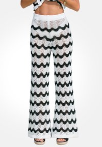 Pantaloni a gamba larga lavorati a maglia con un motivo ondulato bianco e nero, realizzati in un materiale trasparente con una finitura testurizzata. Design con vita elastica.