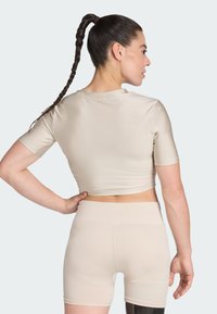 Top corto beige de mangas cortas combinado con pantalones cortos beige sin costuras. Tejido suave y elástico con una silueta ajustada.