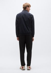 Mereväe kerge jope elastsete varrukate ja vöökohaga, kombineeritud mustade pükste ja beežide tossudega, millel on punased aktsendid.