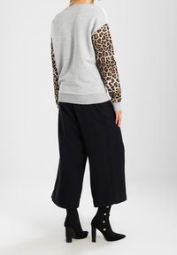 Šedá mikina s rukávy s leopardím potiskem, v kombinaci s černými kalhotami širokého střihu a černými kotníkovými botami se zlatými knoflíky. Jednoduchý design.