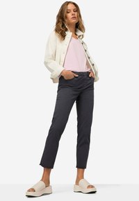 Ivoorkleurige denimjas, lichtroze T-shirt, donkergrijze broek met elastische taille, en beige platform sandalen met een open teen ontwerp.