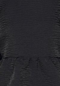 Tissu noir avec une texture froncée créant des plis horizontaux et verticaux ainsi qu’une taille élastique froncée.