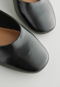 Czarne plastikowe buty o gładkiej fakturze, zaokrąglonym nosku i wycięciu na kostkę, z beżową podszewką.