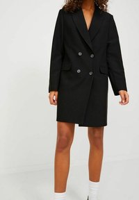 Svart dubbelknäppt kappa gjord av slät tyg, med en vass krage, två framfickor och fyra knappar framtill.