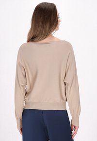 Beige oversized trui met een ronde hals, lange mouwen en geribbelde manchetten, gecombineerd met marineblauwe broek. Glad textuur en een losse pasvorm.