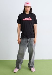 Sort T-shirt med korte ærmer og rødt logo, grå oversized denimbukser og lyserøde sneakers. Lyserød kasket med tekst på forsiden.