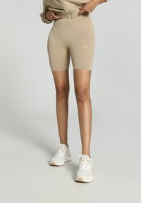 Beige geribbelde fietsshorts met een hoge tailleband, gecombineerd met witte sportschoenen. Soepele textuur, aansluitend ontwerp, subtiele merkdetails.