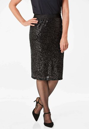 Zwarte sequin kokerrok met een gladde stofafwerking, knielang en een brede tailleband. Gecombineerd met doorschijnende zwarte panty’s en spitse hakken.