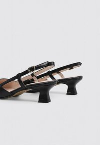 Escarpins noirs à bride de telle avec un petit talon épais, dotés de brides croisées, d'une finition en cuir lisse et d'un détail à boucle sur la sangle de la cheville.