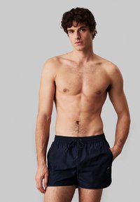 Costumi da bagno navy con vita elastica e cordoncino. Tessuto leggero, texture liscia e tasche laterali per funzionalità.