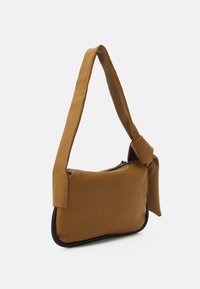 Sac en tissu marron avec un détail de nœud sur la bandoulière, fermeture éclair et un bord noir contrastant en bas. Texture lisse.