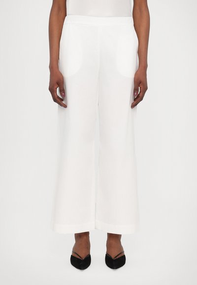 Witte wijde broek met een gladde textuur en een elastische tailleband. Gecombineerd met zwarte puntige schoenen. Voorkant zichtbaar, zonder patronen of accenten.